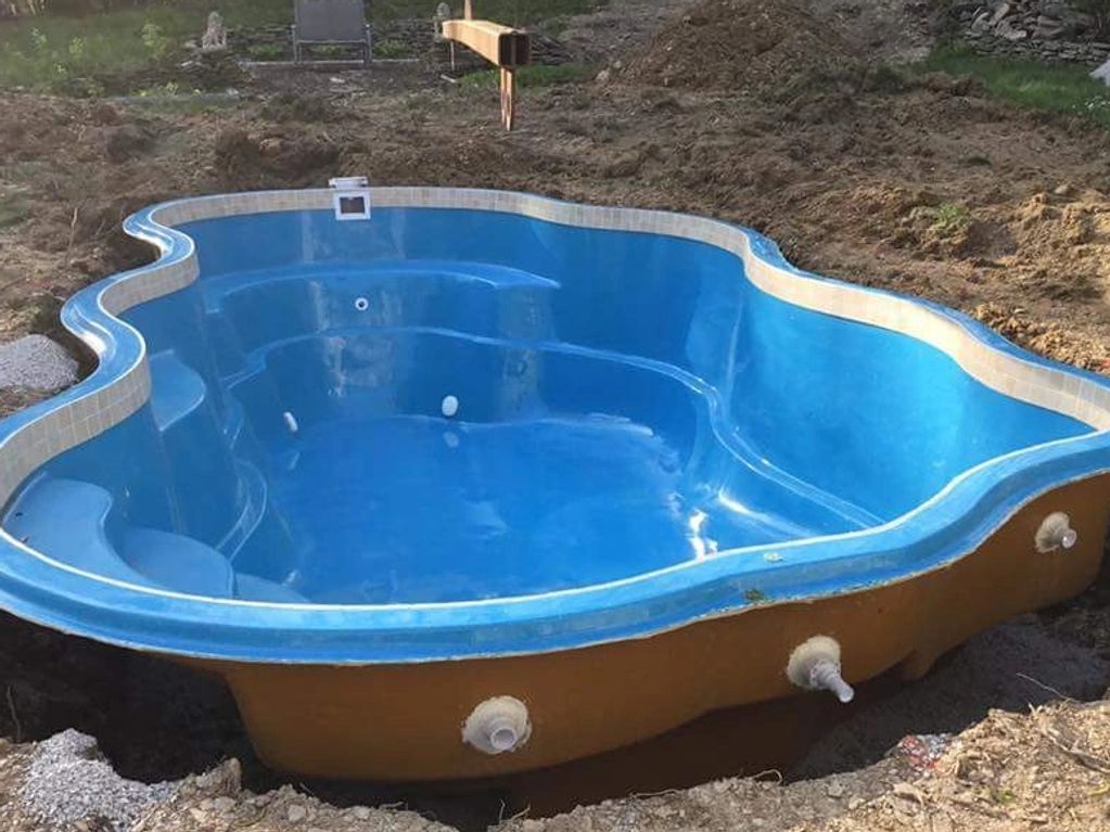 Fiberglass pool shell being lowered and installed into the ground